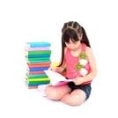 a girl wearing a pink shirt sitting on the floor reading with a stack of books next to her